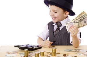 Little boy in black hat and tie at the table counts money, isolated on white